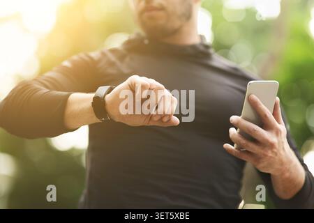 Man Checks Watch While Using Smartphone Outdoors in Sunlight Stock Photo