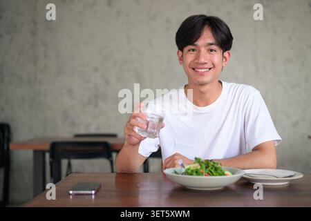Horizontal lifestyle photograph of a handsome young Southeast Asian Thai Isan non-binary man smiling happily and looking directly at the camera while Stock Photo