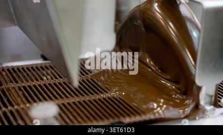 Melted chocolate being poured onto a cooling rack by a chocolate tempering machine in a chocolate factory Stock Photo