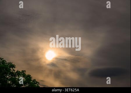 Vibrant sun breaking through dramatic dark clouds in an overcast evening sky. Stock Photo