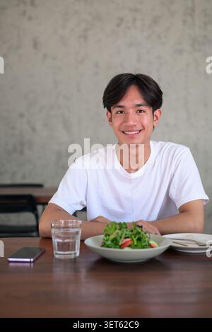 Vertical lifestyle photograph of a handsome young Southeast Asian Thai Isan non-binary man smiling happily and looking directly at the camera while si Stock Photo