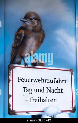 Strange connection between a bird and sign content, a painted bird sitting on a road sign saying keep cleat for fire engines, Stock Photo