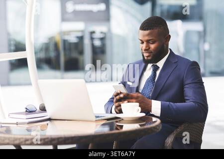 Businessman Sitting at Outdoor Cafe Using Smartphone During Work Hours in Sunny Weather Stock Photo