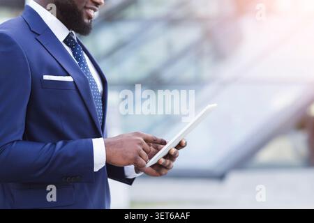 A Man Dressed in a Suit Interacts With a Tablet While Standing in an Urban Area Stock Photo