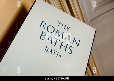 A clean, modern white signboard featuring the elegant dark typography for 'The Roman Baths, Bath'. The shot is taken at a dynamic diagonal angle showi Stock Photo
