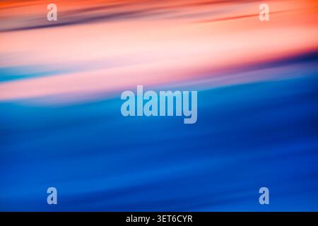 Soft blue and orange gradients flow in diagonal motion blur, creating an abstract, calming background that evokes sunset reflections on water. Ideal f Stock Photo