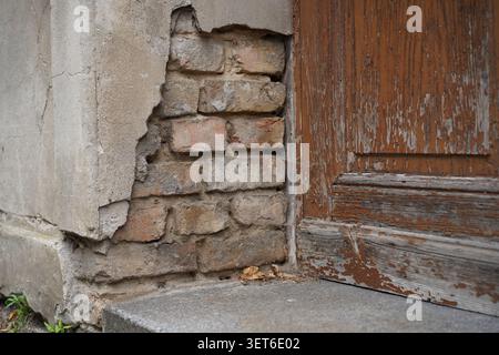 Close-up of a weathered historic building facade with damaged plaster, exposed brickwork and old wooden door at Neuer Markt in Potsdam, Germany. Stock Photo