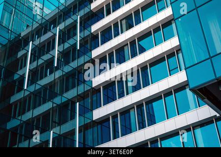 Architectural shot of a contemporary multi-story office building with blue-tinted glass curtain wall and white structural panels. Selective focus. Stock Photo