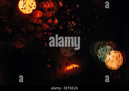 Moody rainy night scene of raindrops on a window with colorful bokeh city lights reflected and blurred, selective focus Stock Photo