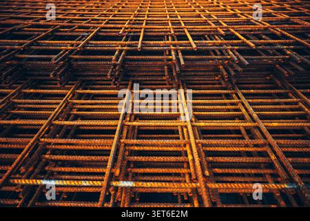 Rusted steel rebar mesh stacked at a construction site, forming a repetitive geometric pattern. Industrial building materials, engineering and infrast Stock Photo