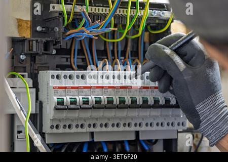 Utrecht, Netherlands - June 01, 2026: Close-up of an electrician using a marker to label new ABB circuit breakers inside a home electrical fuse box du Stock Photo