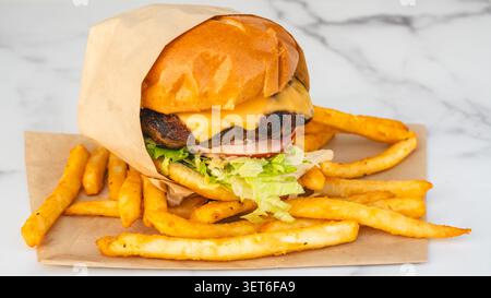 Loaded cheeseburger with melted cheddar, lettuce, tomato, onion, and sauce served with seasoned french fries on butcher paper. Stock Photo