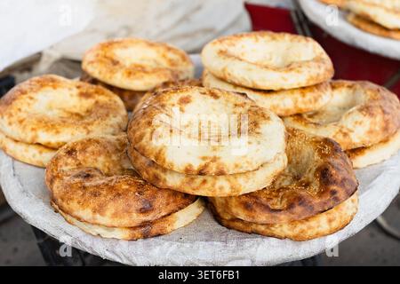 Fresh hot flatbreads piled high on street vendor tray. Golden crusty  freshly baked traditional central asian bread lepyoshka or naan at stall in sunn Stock Photo