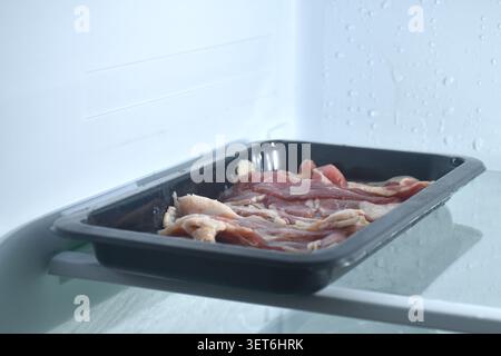 raw frozen beef meat slice roll ingredient food on black plastic tray in refrigerator Stock Photo