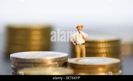Miniature figurine of construction manager / architect on stacks of coins, concept of construction budget, project investment and building costs Stock Photo