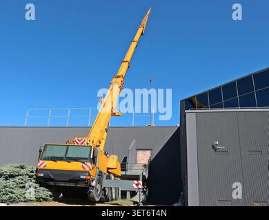 Yellow telescopic crane on a large truck working outside a modern gray building Stock Photo