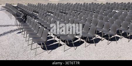 Long rows of empty gray plastic chairs geometrically arranged under the sun. Side view, Background for copy space. Stock Photo
