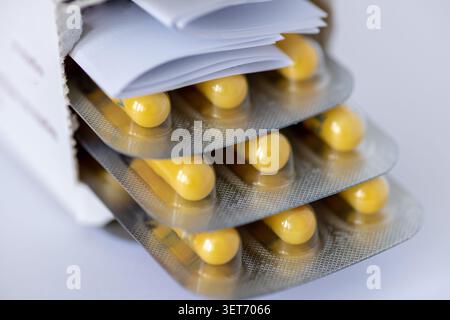 A close up of an opened box of medicine showing the yellow capsules in blister packs and the instructions inside. Stock Photo