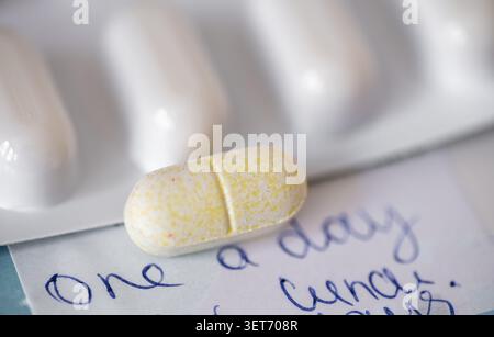 A close up of a medicine blister pack and an individual pill tablet on top of a box of medication with the words one a day on the packaging. Stock Photo