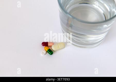 Various medicine tablets and capsules next to a glass of water isolated on white. Stock Photo