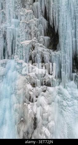 Aerial view of a massive frozen waterfall with intricate icicles and layers of ice covering the rugged mountain rock face in Khunjerab National Park, Stock Photo