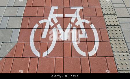 A high angle view of a stenciled white bicycle icon on a reddish brown interlocking brick lane flanked by grey stone pavers and textured tactile Stock Photo