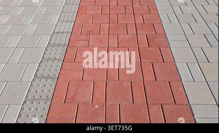 A linear perspective shot of a modern urban walkway showing a central red block paving strip separated from a grey pedestrian sidewalk by a textured Stock Photo