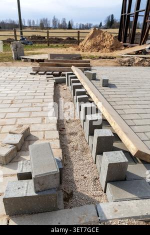 Close-up view of workers laying grey paving blocks on a construction site. Piles of bricks and tools around. Stock Photo