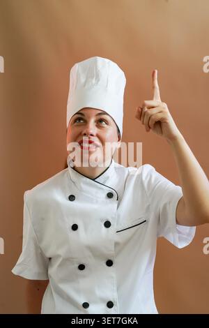 Female chef in white uniform looking up, pointing finger to an idea space Stock Photo