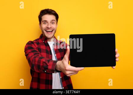 Happy Young Caucasian Man Holding Blank Tablet With Smile, Yellow Background, Mockup Stock Photo