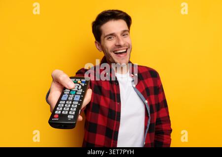Smiling Young Caucasian Man Holding Remote Control At Home, Yellow Background Stock Photo
