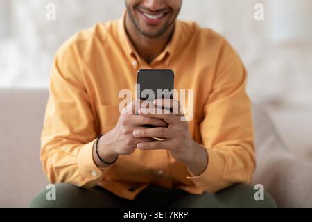 Smiling Young Man Using Smartphone At Home, Relaxed Lifestyle Concept Stock Photo