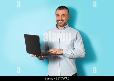 Smiling Man Holding Laptop, Standing Against Blue Background, Business Concept Stock Photo