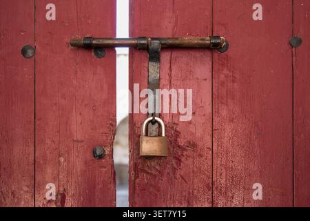 Close-up of a padlock securing an antique vintage red wooden door with wrought iron detailing Stock Photo