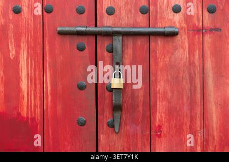 Close-up of a padlock securing an antique vintage red wooden door with wrought iron detailing Stock Photo