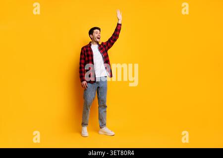 Happy Young Caucasian Man Waving Hand In Studio, Yellow Background Stock Photo