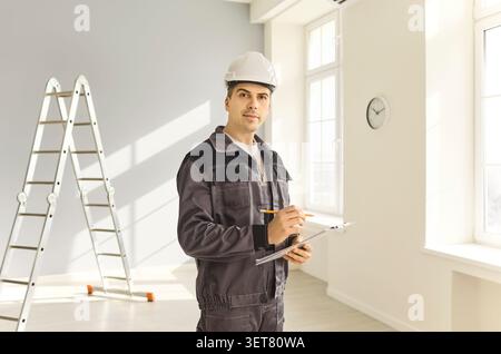 Contractor in safety helmet with clipboard assessing light modern home interior Stock Photo