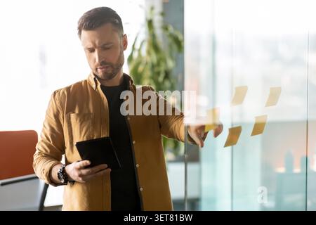 Focused Caucasian Male Professional Analyzing Data On Tablet In Modern Office, Business Concept Stock Photo