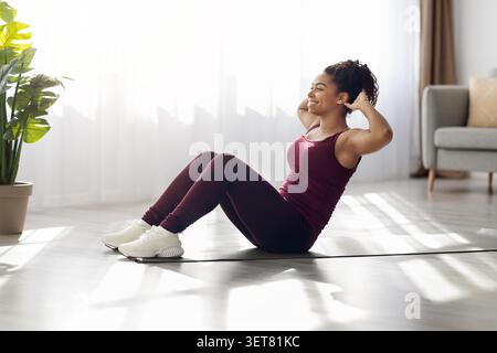 Happy Black Woman Exercising On Mat At Home, Engaging In Fitness Routine, Weight Loss Concept Stock Photo