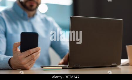 Businessman Using Smartphone In Office While Working On Laptop, Focused And Productive Stock Photo