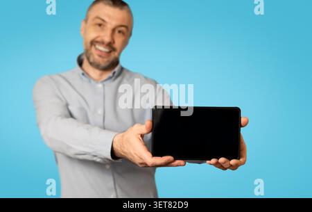 Smiling Man Holding Tablet With Blank Screen, Blue Background, Technology Concept Stock Photo