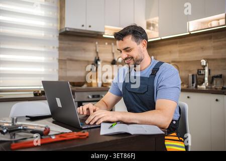 Repairman working on laptop in kitchen with plumbing tools Stock Photo