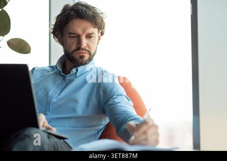 Focused Caucasian Male Working From Home, Taking Notes In Modern Office Setting, Business Concept Stock Photo