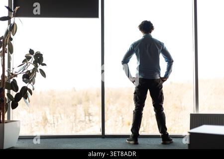 Unrecognizable Man Standing Near Window, Contemplating Indoor Office Setting, Business Concept Stock Photo