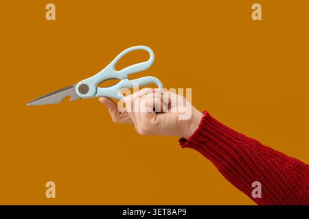 Hand holding light blue kitchen shears with bottle opener feature on warm orange background, the versatile kitchen tool features sharp metal blades an Stock Photo