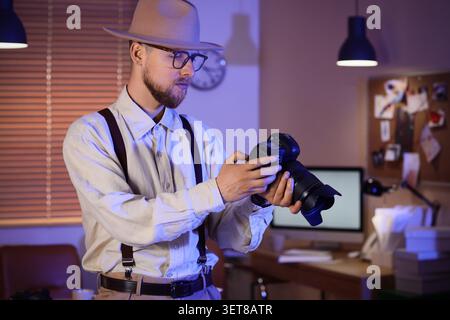 Professional photographer adjusting DSLR camera settings in home office studio at night, creative photography workflow Stock Photo