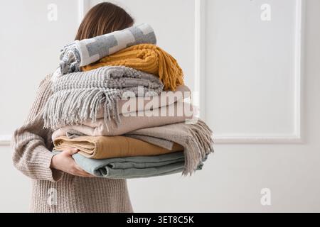 Woman with stack of plaids near light wall Stock Photo