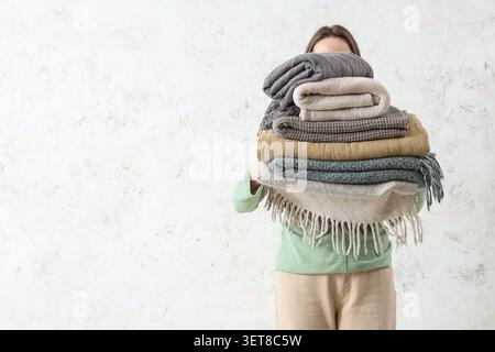 Woman with stack of plaids on light grunge background Stock Photo