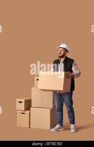 Smiling male worker in hard hat and vest carrying cardboard box, moving and delivery service Stock Photo