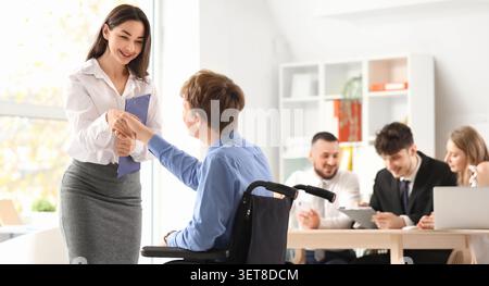 Businesswoman shaking hands with disabled man in wheelchair during office meeting, inclusive workplace environment Stock Photo